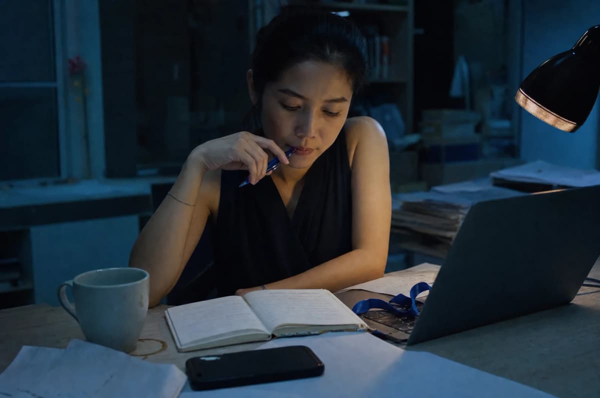 ผู้สมัครงานนั่งเขียนรายการทักษะและจุดแข็งของตัวเองลงสมุดโน้ตที่โต๊ะทำงานตอนค่ำ